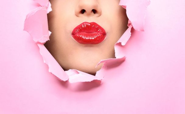 View of beautiful young woman with red lips through hole in color paper, closeup - Foto, Imagen