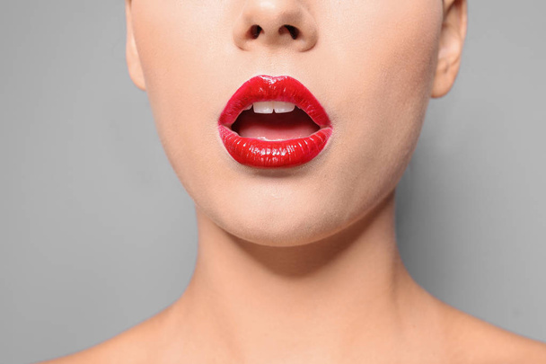 Beautiful young woman with red glossy lips on gray background, closeup - Φωτογραφία, εικόνα
