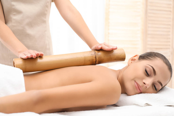 Young woman having massage with bamboo stick in wellness center - Photo, Image