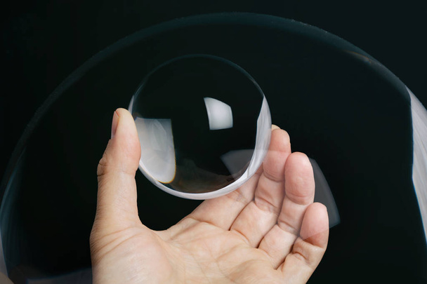 Hand holding a transparent crystal ball with black background. - Fotó, kép
