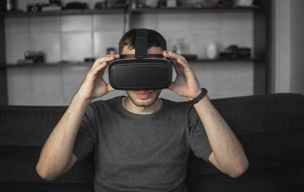 Young bearded man wearing headset of virtual reality in office sitting on a sofa. - Photo, Image