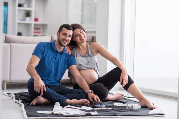 счастливая беременная пара проверяет список вещей для их нерожденного ребенка дома на полу
 - Фото, изображение