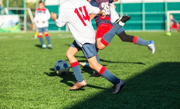 Fußballmannschaften - Jungen in roter, blauer und weißer Sportbekleidung spielen Fußball auf dem grünen Feld. Jungen dribbeln. Dribbelkünste. Teamspiel, Training, aktiver Lebensstil, Hobby, Sport für Kinder Konzept - Foto, Bild