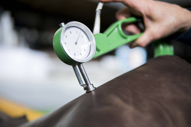 Woman hands use Leather thickness gauge on with a natural brown leather. Preparing of the raw materials for manufacture of bags, shoes, clothing and accessories. - Photo, image
