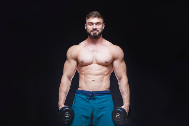 Muscular bodybuilder guy doing exercises with dumbbell over black background - Fotografie, Obrázek