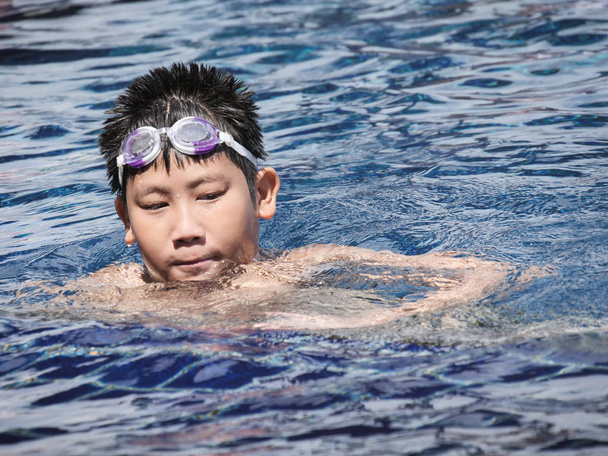 Asiatico ragazzo indossare occhiali e nuotare in piscina in giornata di sole
. - Foto, immagini