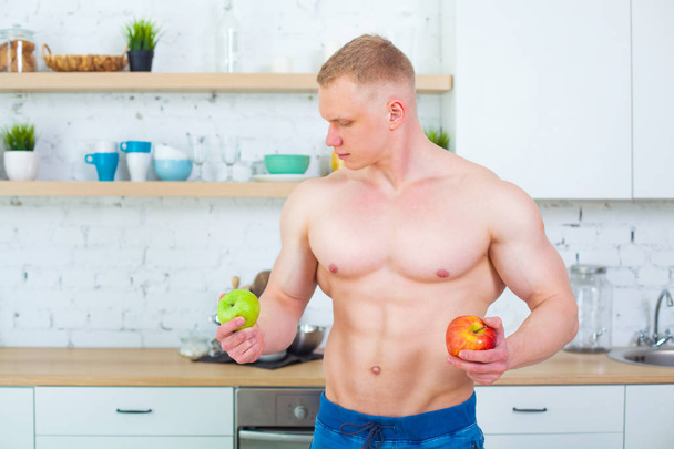 Gespierde man met een naakte torso in de keuken met fruit, begrip van gezond eten. Atletische manier van leven. - Foto, afbeelding