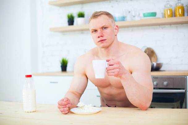 Muscular man with a naked torso in the kitchen with milk and cottage cheese, the concept of a healthy diet. Athletic way of life. - Foto, Imagen
