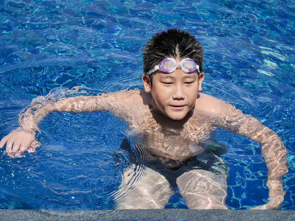 Asian boy wearing goggles and swimming in pool in sunny day. - Photo, Image