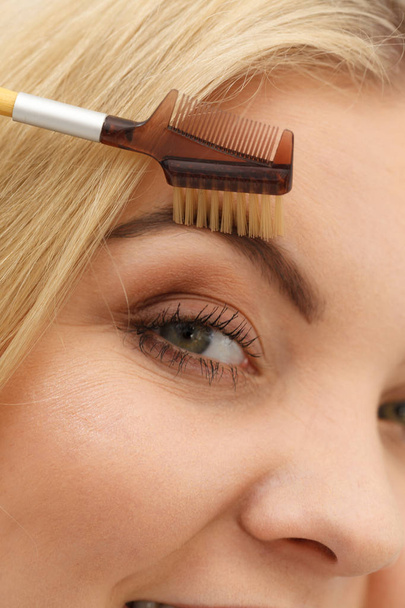 Close up of woman doing her make up, preparing brows using brush tool brushing eyebrows. - Фото, зображення