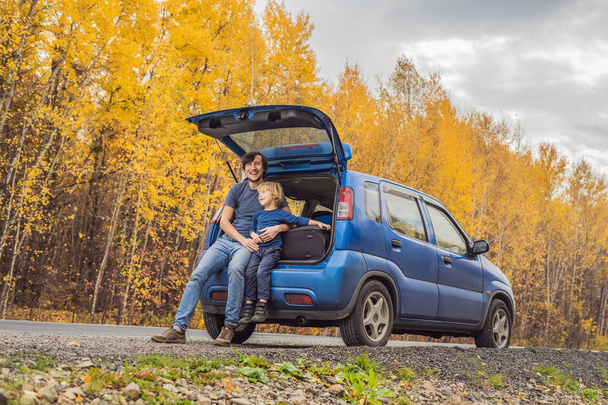 Father and son resting on roadside in car trunk while road trip in autumnal woodland. - Фото, зображення