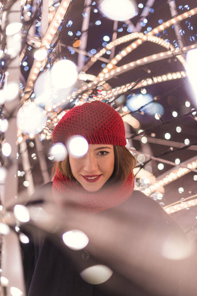 Red hat girl standing inside  christmas tree lights at night - Foto, imagen