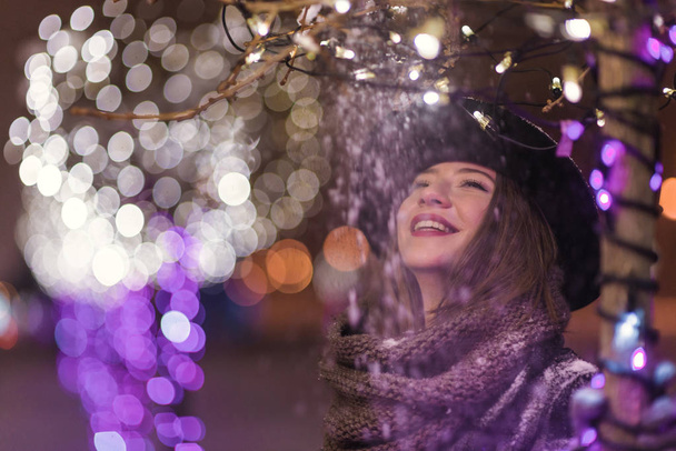 Giovane ragazza in piedi davanti alle luci dell'albero di Natale di notte con fiocchi di neve che cadono, nevicando
 - Foto, immagini