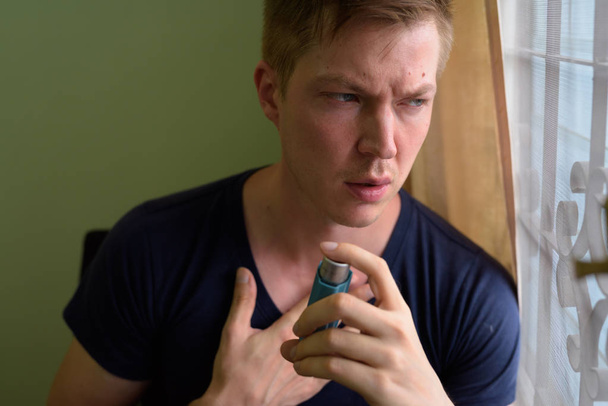 Νεαρός όμορφος άντρας που χρησιμοποιεί συσκευή εισπνοής άσθματος στο σπίτι - Φωτογραφία, εικόνα