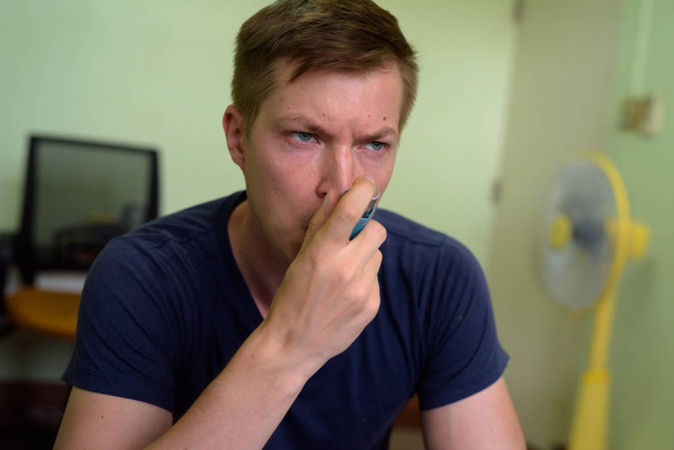 Young handsome man using asthma inhaler at home - Foto, Imagen