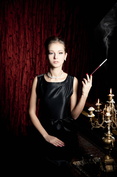 dame élégante avec coiffure élégante fumer à côté chandelier vintage avec des bougies brûlantes
  - Photo, image