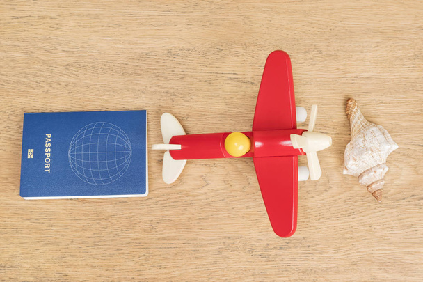 Passport, toy plane and shell lying on a wooden table as a concept of relaxing by the sea - Photo, Image