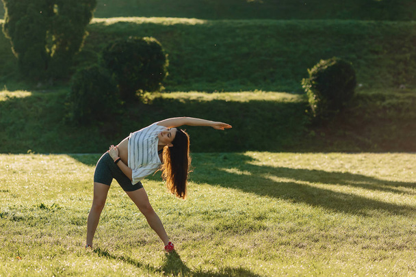 cozy fitness girl making morning stretching exercises outside on sunshine an grass - Fotoğraf, Görsel