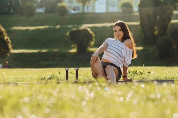 cozy fitness girl making exercises with dumbbells on sunset at grass outside - Photo, Image