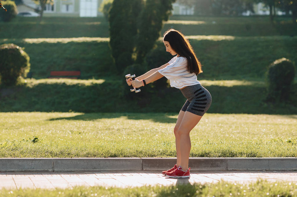 затишна фітнес дівчина робить вправи з гантелями на заході сонця на траві зовні
 - Фото, зображення