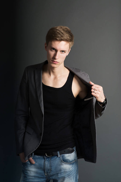 Retrato de hombre joven serio en camiseta negra y elegante chaqueta posando sobre fondo gris
 - Foto, Imagen