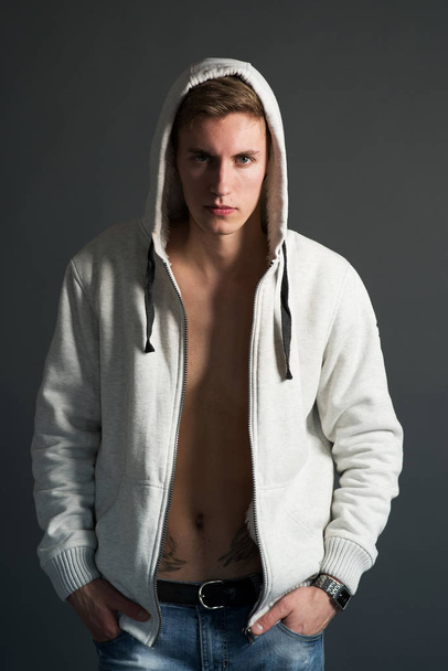 Young man with naked tattooed torso in white hoodie posing on black background  - Fotografie, Obrázek