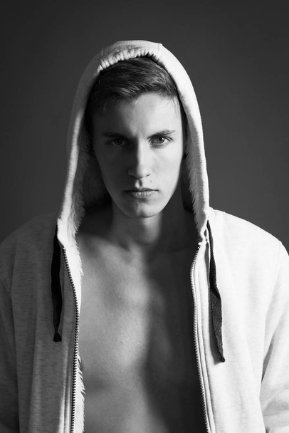Portrait of serious young man with naked torso in white hoodie posing on black background  - Foto, Imagen