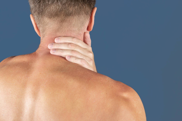 Man holding his neck in pain, isolated on blue background. Lower neck pain. Shirtless man touching his neck for the pain - Photo, Image