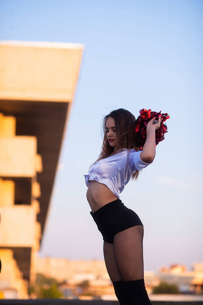 cheerleader with pompoms dancing outdoors on the roof at sunset - Фото, зображення