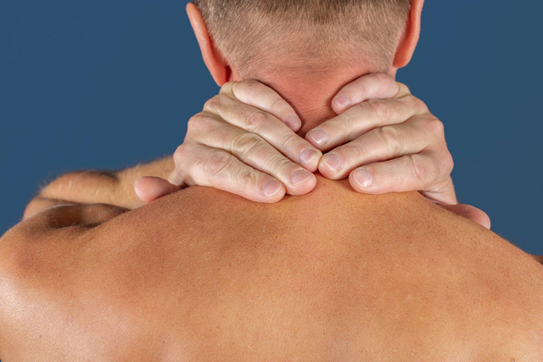 Man met zijn nek pijn, geïsoleerd op blauwe achtergrond. Lagere nekpijn. Shirtless man zijn hals raken voor de pijn - Foto, afbeelding