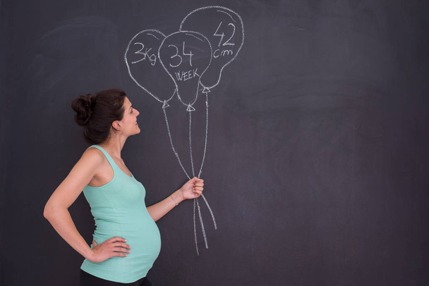 Portrait of happy pregnant woman with hands on belly in front of black chalkboard - Foto, Imagem