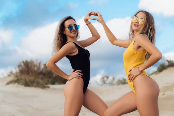 Couple of sexy girls posing at the beach, show the heart symbol with their hands. - Фото, зображення