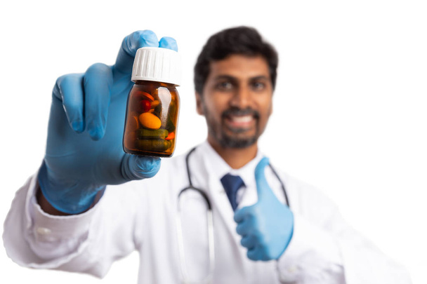 Pills in bottle recommended by smiling indian medic with trustworthy expression holding thumb up as agree gesture isolated on white - Fotoğraf, Görsel