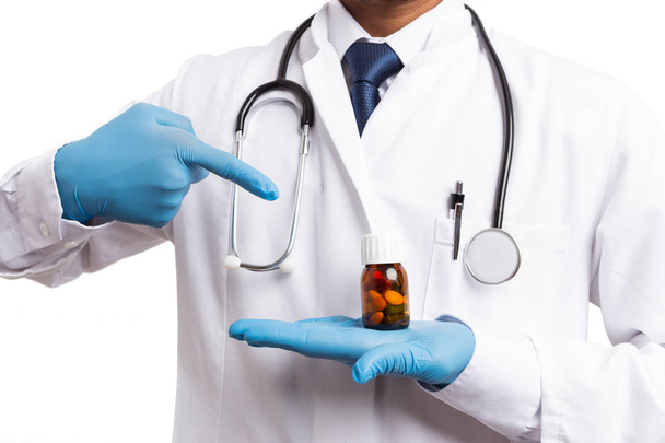 Indiase medic blauw handschoenen wijzend op pil fles met wijsvinger geïsoleerd op witte achtergrond - Foto, afbeelding