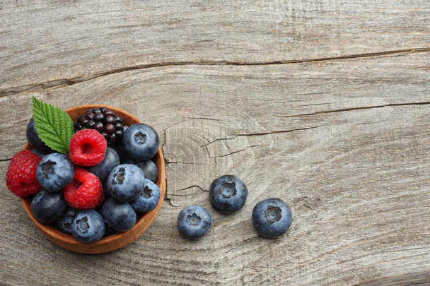 mix of blueberries, blackberries, raspberries in wooden bowl on old wooden table background. top view with copy space - Photo, image