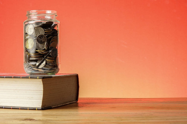 FONDO DE EDUCACIÓN CONCEPTO con monedas en un frasco de vidrio y libro viejo
. - Foto, Imagen