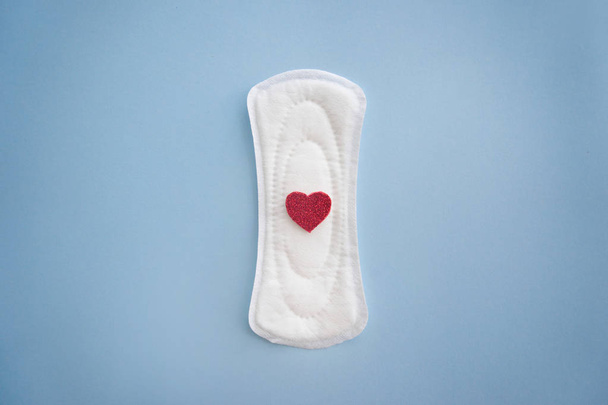 Менструальная прокладка с красным сердцем на цветном фоне
 - Фото, изображение