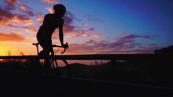 Silhouet van een man die een fiets bij zonsondergang op een berg weg-zijaanzicht. Slow motion steadicam - Video