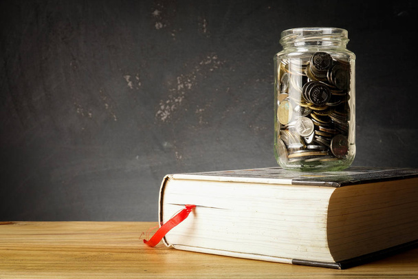 Έννοια Ταμείο εκπαίδευσης με κέρματα σε ένα γυάλινο βάζο και το παλιό βιβλίο. - Φωτογραφία, εικόνα
