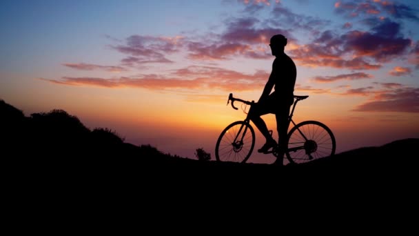 Νέος σπορ άνδρας κάθεται σε ένα ποδήλατο στην κορυφή ενός βουνού σε ένα κίτρινο κράνος t-shirt και αθλητικός εξοπλισμός, κοιτάζοντας το ηλιοβασίλεμα. Αργή κίνηση steadicam - Πλάνα, βίντεο