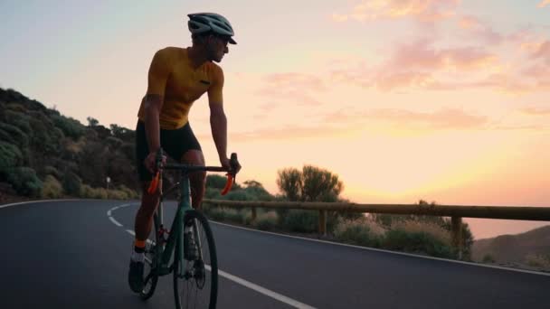 Bir genç spor adamı bir dağda serpantin bir bisiklet sürmek ve sarı bir tişört ve spor ekipmanları kamerada bakar. Ağır çekim steadicam - Video, Çekim