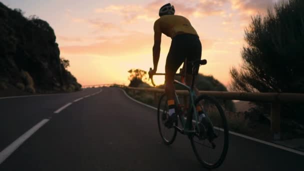 A young sports man riding a bike on a mountain serpentine in a yellow t-shirt helmet and sports equipment rear view . Slow motion steadicam - Footage, Video