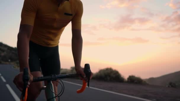 Bir genç spor adamı bir dağda serpantin bir bisiklet sürmek ve sarı bir tişört ve spor ekipmanları kamerada bakar. Ağır çekim steadicam - Video, Çekim