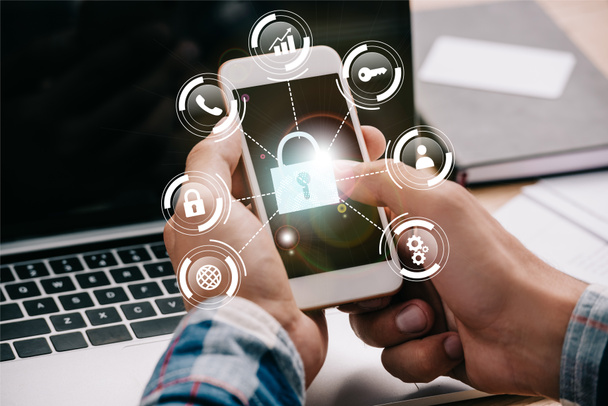 Oříznout záběr podnikatel pomocí smartphone s cyber bezpečnostní značky na pracovišti s notebookem - Fotografie, Obrázek