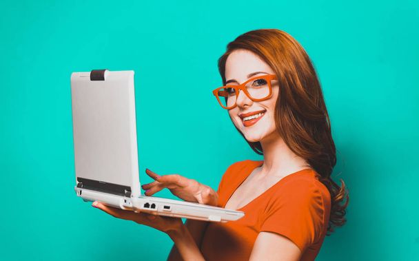 Kızıl saçlı kız ile mavi arka plan üstünde laptop. - Fotoğraf, Görsel