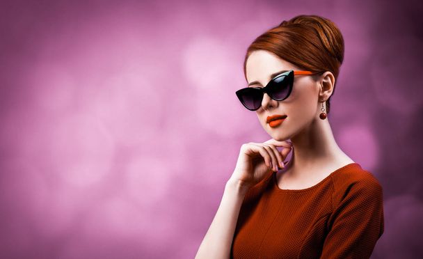 Beautiful redhead woman in sunglasses on viloet background. - Photo, Image
