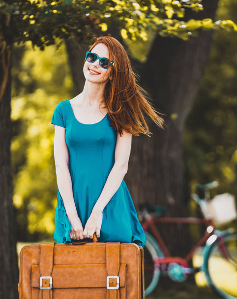 Redhead girl with suitcase in the park. Summertime season - Zdjęcie, obraz