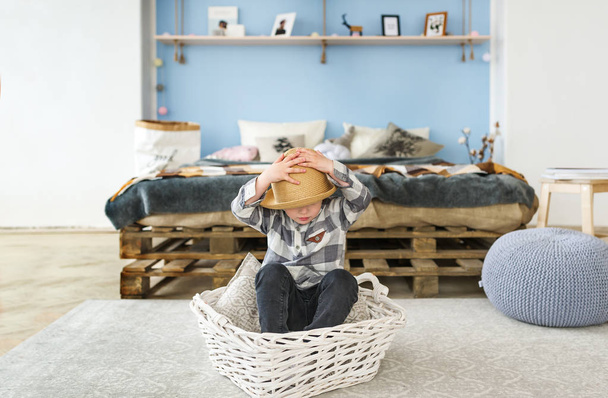 Cute little boy in straw hat sitting in the big basket at bedroom - Photo, Image