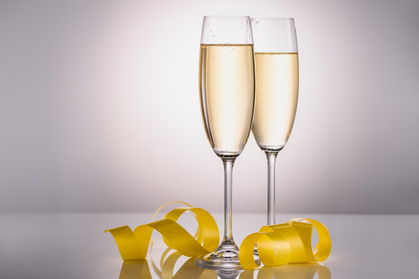 close up view of glasses of champagne and yellow festive confetti on grey background - Foto, afbeelding