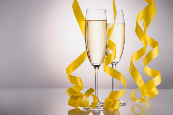 close up view of glasses of champagne and yellow festive confetti on grey background - Zdjęcie, obraz